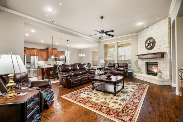 living room with a stone fireplace, dark hardwood / wood-style floors, ceiling fan with notable chandelier, and ornamental molding