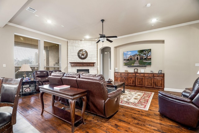 living room with dark hardwood / wood-style floors, ceiling fan, a stone fireplace, and crown molding