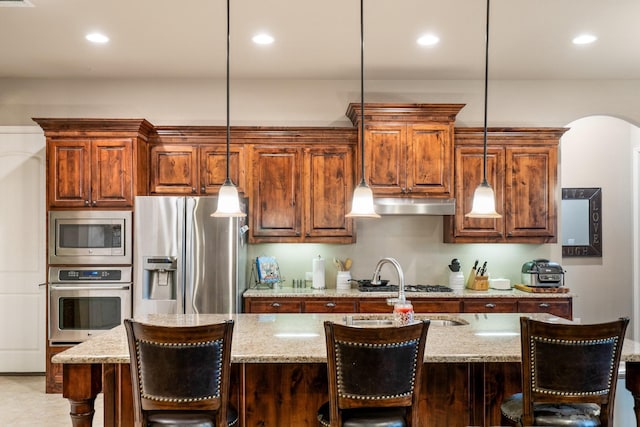 kitchen featuring a center island with sink, decorative light fixtures, light stone countertops, and appliances with stainless steel finishes