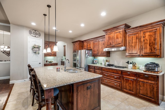 kitchen featuring sink, hanging light fixtures, light stone counters, a center island with sink, and appliances with stainless steel finishes