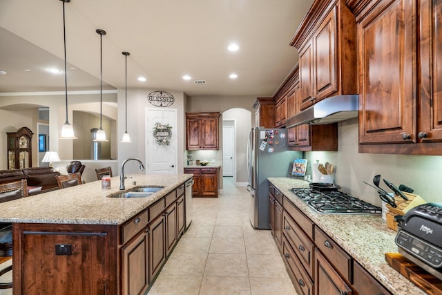 kitchen with sink, hanging light fixtures, stainless steel appliances, light stone counters, and a kitchen island with sink