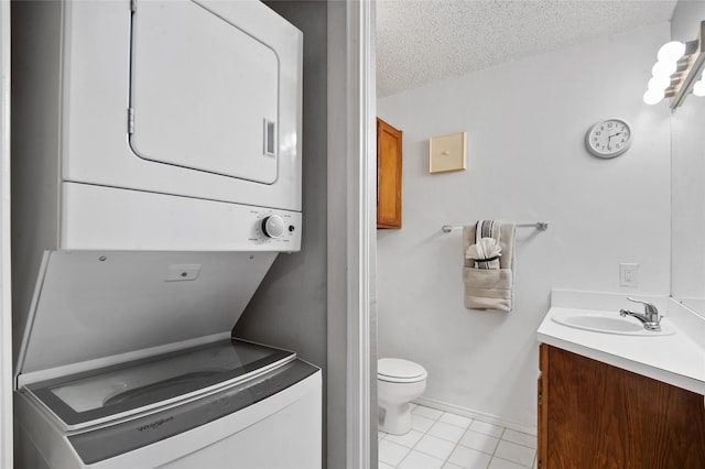 bathroom featuring stacked washer / dryer, toilet, tile patterned floors, vanity, and a textured ceiling