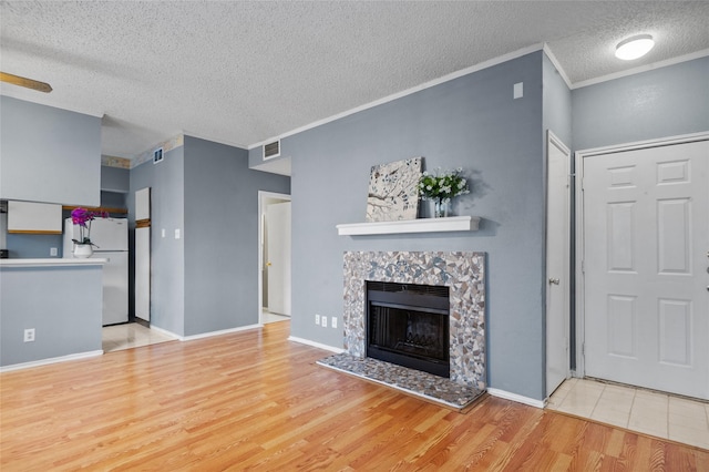 unfurnished living room featuring a textured ceiling, a tiled fireplace, ceiling fan, ornamental molding, and light hardwood / wood-style floors