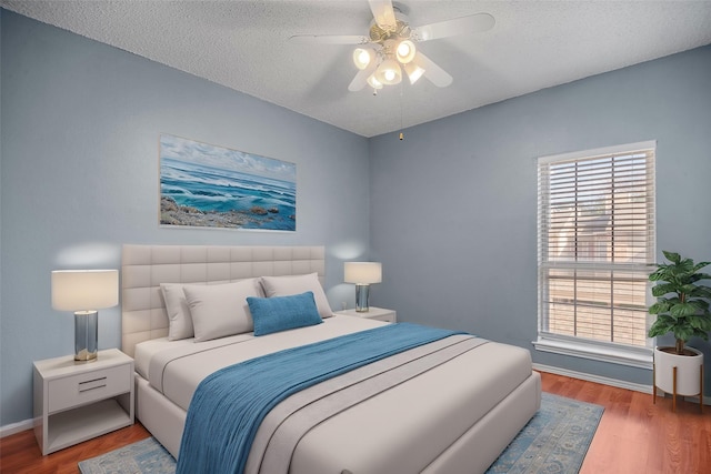 bedroom with hardwood / wood-style flooring, a textured ceiling, ceiling fan, and multiple windows