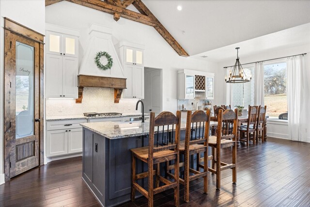 kitchen with light stone countertops, vaulted ceiling with beams, decorative light fixtures, and white cabinetry