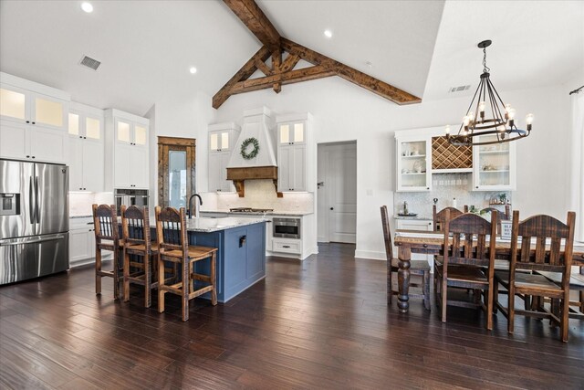 kitchen with pendant lighting, an island with sink, beamed ceiling, white cabinetry, and stainless steel appliances