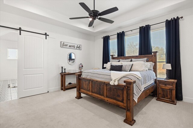 bedroom with ceiling fan, a barn door, a raised ceiling, and light colored carpet