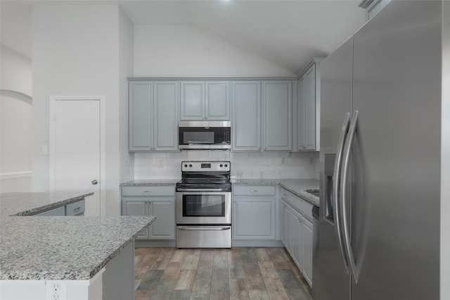 kitchen featuring lofted ceiling, hardwood / wood-style flooring, gray cabinets, appliances with stainless steel finishes, and tasteful backsplash