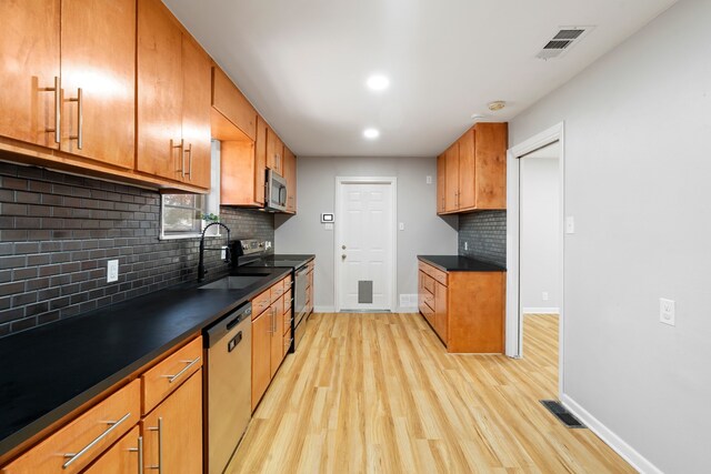 kitchen featuring decorative backsplash, appliances with stainless steel finishes, light wood-type flooring, and sink