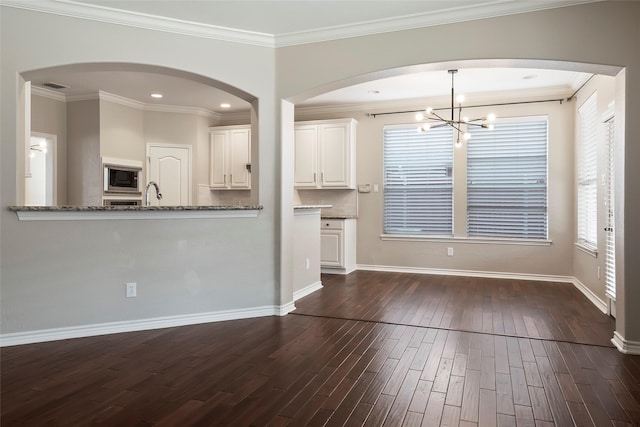 unfurnished living room featuring sink, dark hardwood / wood-style flooring, crown molding, and an inviting chandelier