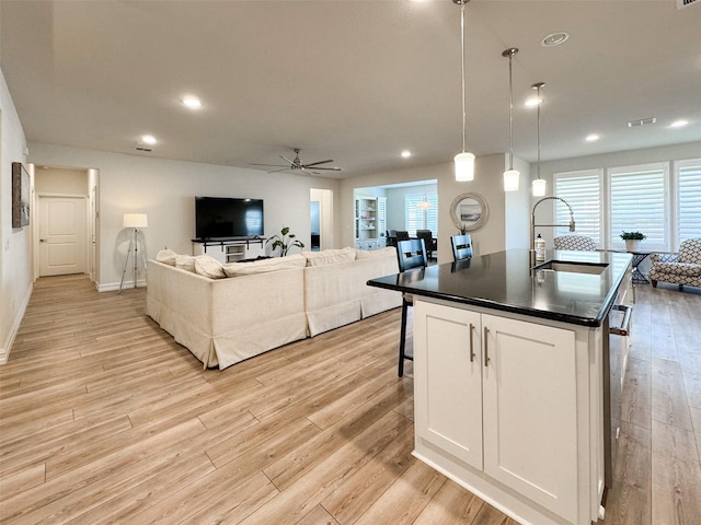 kitchen with white cabinetry, sink, ceiling fan, hanging light fixtures, and a center island with sink