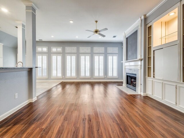 unfurnished living room with wood-type flooring, decorative columns, built in features, and ceiling fan