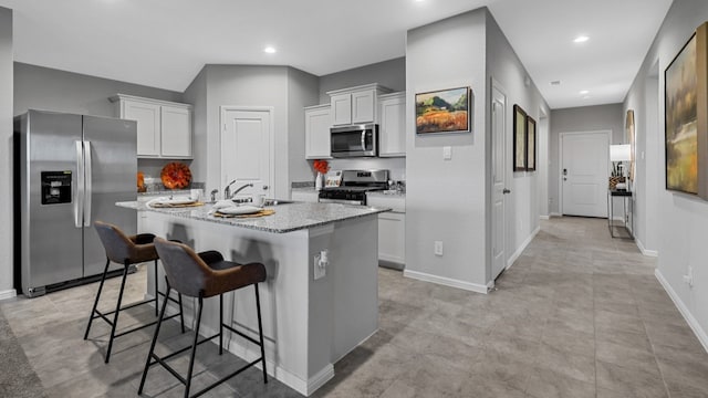 kitchen featuring light stone countertops, a breakfast bar area, a center island with sink, white cabinets, and appliances with stainless steel finishes