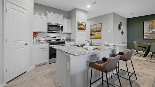 kitchen featuring white cabinetry, sink, stainless steel appliances, a kitchen bar, and a center island with sink