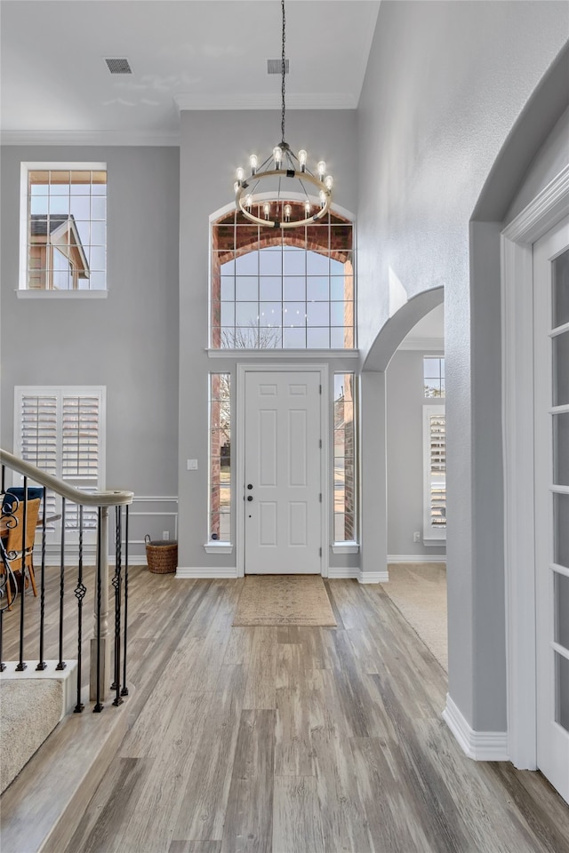 entryway with hardwood / wood-style floors, a towering ceiling, ornamental molding, and a notable chandelier