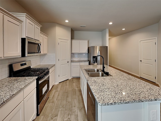 kitchen with a kitchen island with sink, white cabinets, sink, light hardwood / wood-style floors, and stainless steel appliances