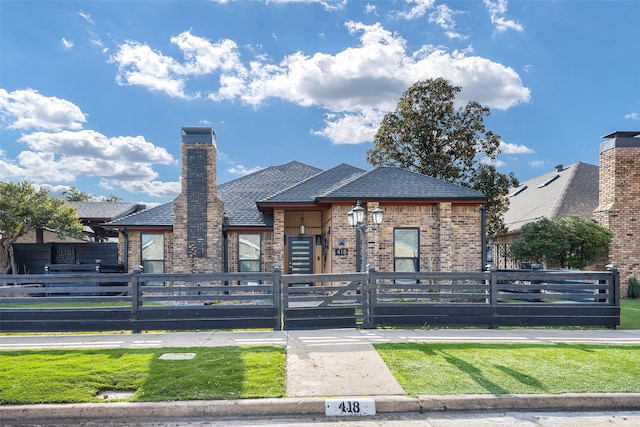 view of front facade with a fenced front yard, a chimney, brick siding, and a shingled roof