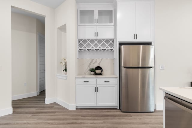 kitchen with white cabinets, appliances with stainless steel finishes, light hardwood / wood-style flooring, and light stone countertops