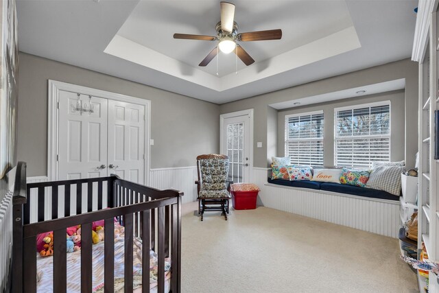 carpeted bedroom featuring a crib, a closet, a raised ceiling, and ceiling fan