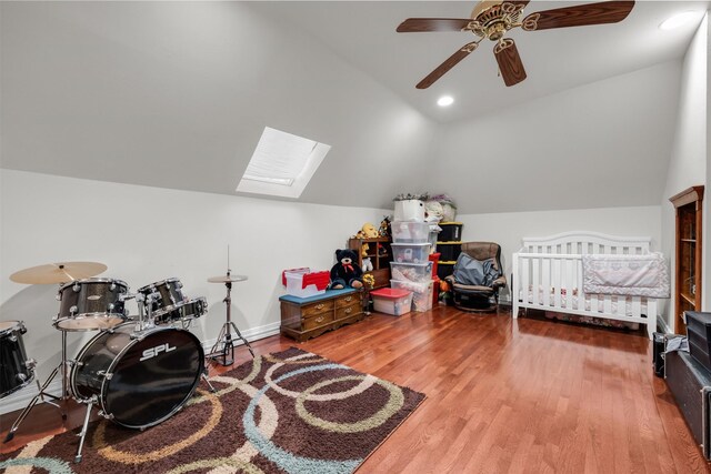 bedroom with ceiling fan, wood-type flooring, a nursery area, and lofted ceiling with skylight