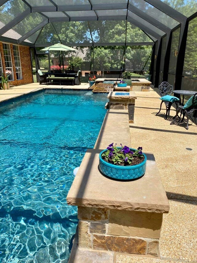 view of pool with glass enclosure, an in ground hot tub, and a patio