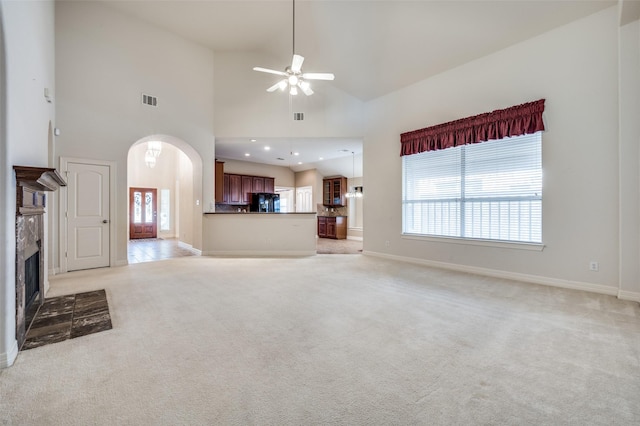 unfurnished living room with a towering ceiling, ceiling fan, a tile fireplace, and light carpet