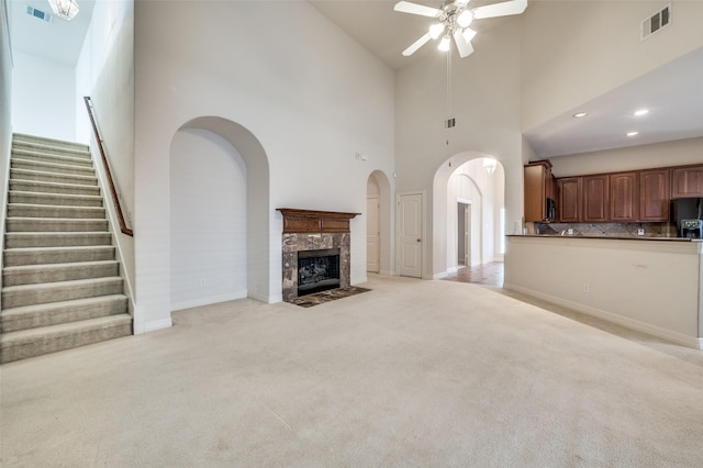 unfurnished living room featuring ceiling fan, a high ceiling, light colored carpet, and a high end fireplace