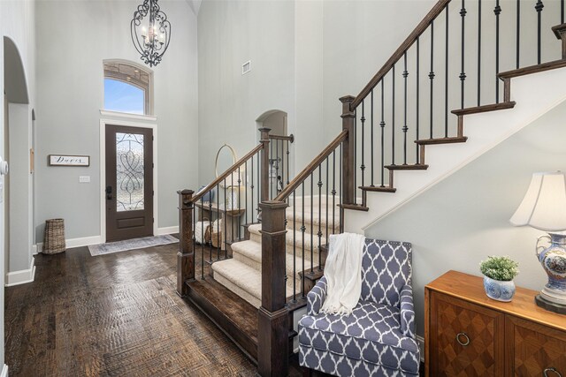 entryway featuring a towering ceiling, dark wood-type flooring, and a notable chandelier