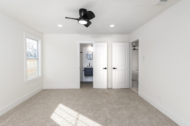 unfurnished bedroom featuring ceiling fan, ensuite bathroom, and light carpet