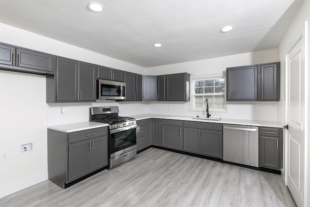 kitchen featuring sink, stainless steel appliances, a textured ceiling, gray cabinets, and light wood-type flooring