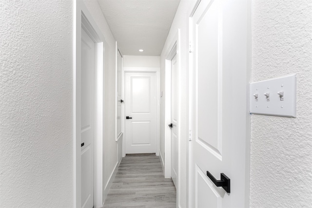 hallway with a textured ceiling and light wood-type flooring