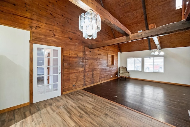 interior space with lofted ceiling with beams, wood-type flooring, a notable chandelier, and wood walls