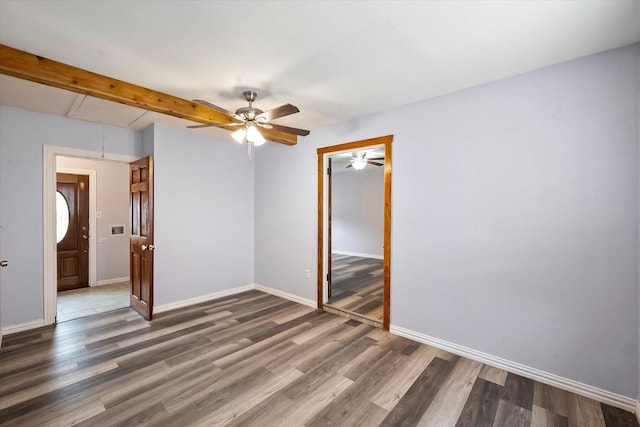 unfurnished room with ceiling fan, dark wood-type flooring, and beam ceiling