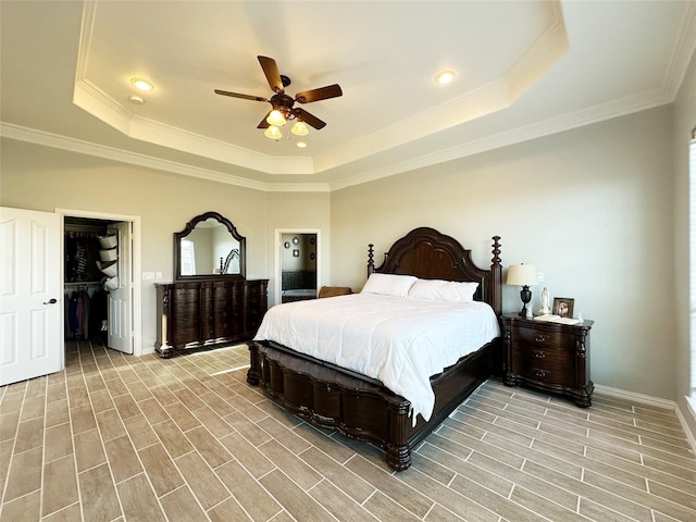 bedroom with ceiling fan, a raised ceiling, and a walk in closet