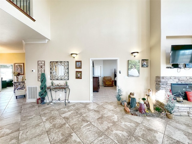 interior space with a stone fireplace, a towering ceiling, and crown molding