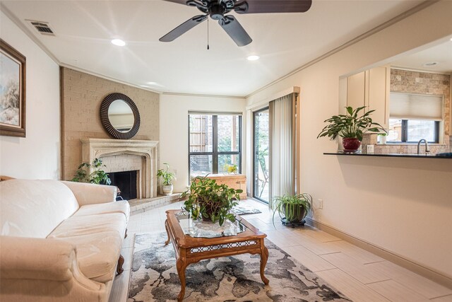 living room featuring ceiling fan, sink, crown molding, and a brick fireplace