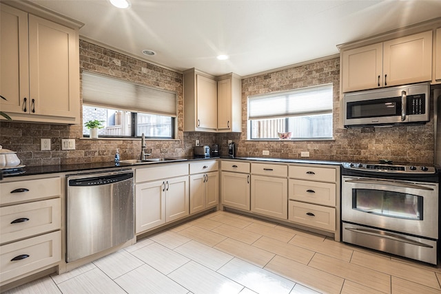 kitchen with appliances with stainless steel finishes, tasteful backsplash, cream cabinets, and sink