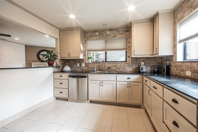 kitchen with dark stone countertops, cream cabinets, sink, and stainless steel dishwasher