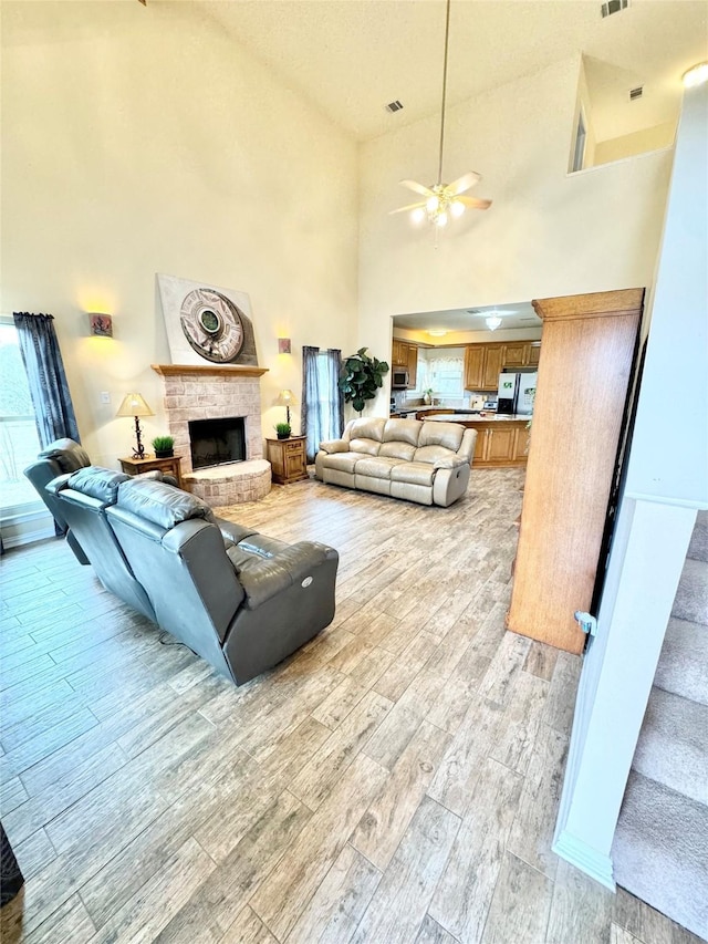 living room featuring a brick fireplace, light hardwood / wood-style flooring, ceiling fan, and a high ceiling