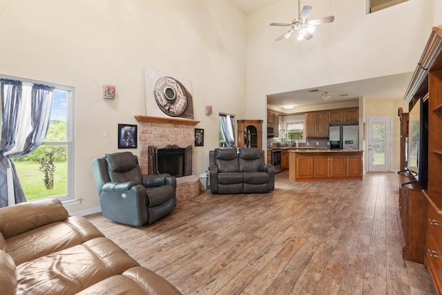 living room featuring a fireplace, a high ceiling, light hardwood / wood-style flooring, and ceiling fan