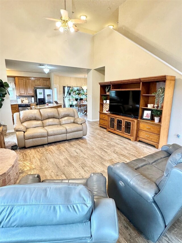 living room with ceiling fan, light hardwood / wood-style flooring, and a towering ceiling