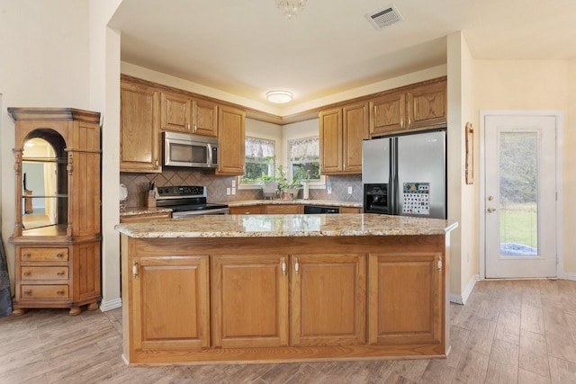 kitchen featuring light stone counters, appliances with stainless steel finishes, decorative backsplash, a kitchen island, and light wood-type flooring