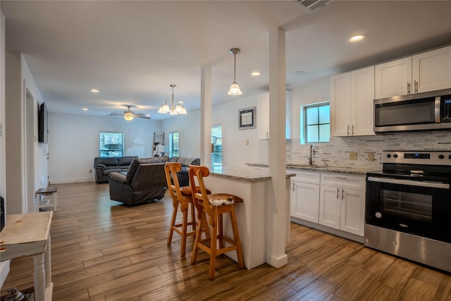 kitchen featuring pendant lighting, a breakfast bar area, appliances with stainless steel finishes, light stone counters, and white cabinets