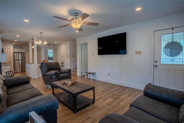 living room with light hardwood / wood-style floors and ceiling fan with notable chandelier