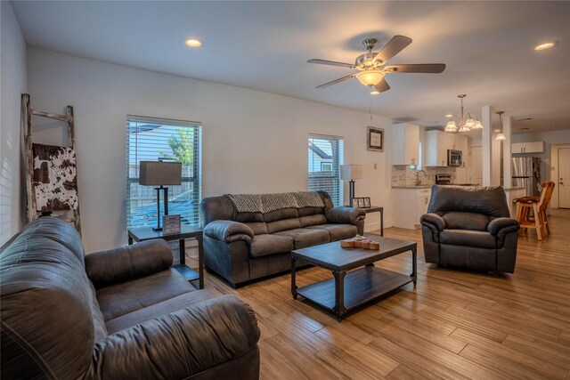 living room featuring ceiling fan with notable chandelier and light hardwood / wood-style flooring