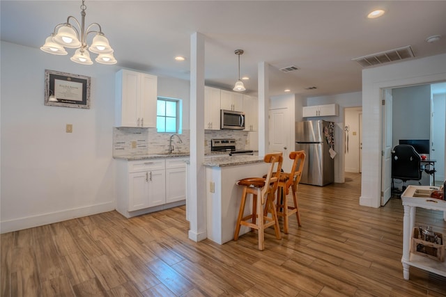 kitchen featuring pendant lighting, white cabinetry, sink, light hardwood / wood-style floors, and stainless steel appliances