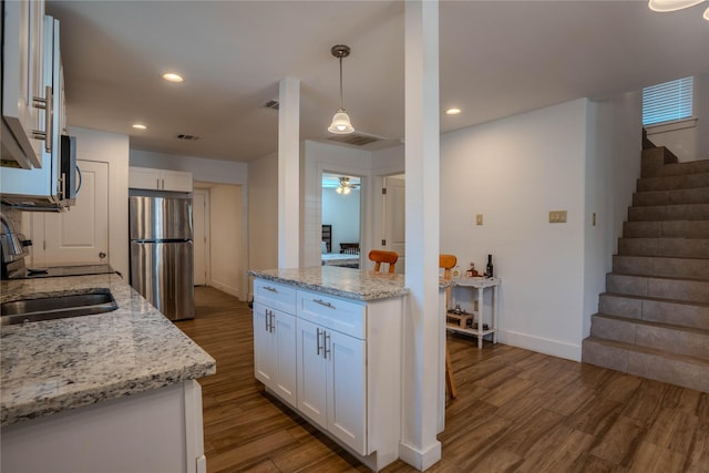 kitchen with stainless steel refrigerator, light stone countertops, sink, and white cabinets