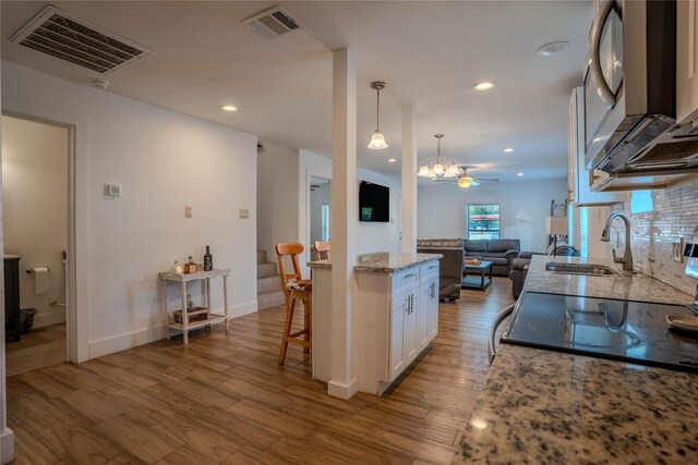 kitchen featuring sink, white cabinetry, hanging light fixtures, light stone countertops, and light hardwood / wood-style floors