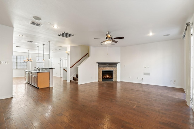 unfurnished living room with dark hardwood / wood-style floors, sink, a fireplace, and ceiling fan with notable chandelier