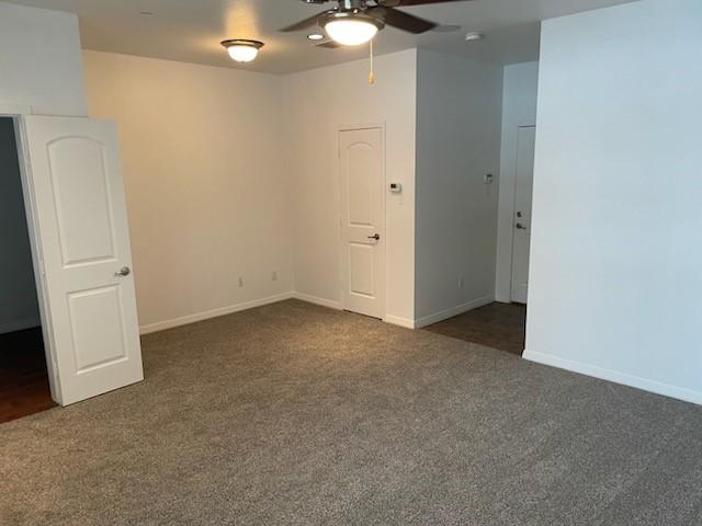 empty room with dark colored carpet and ceiling fan